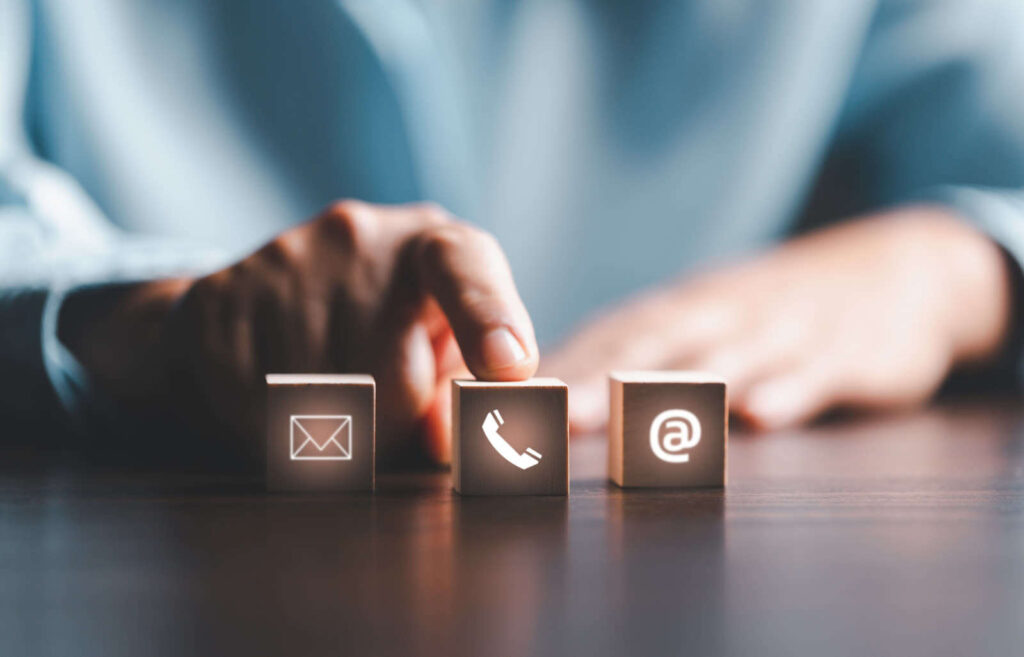Hand choosing a contact channel on wooden cubes with mail, phone and at symbols